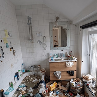 Salle de bains remplie d'objets et de détritus avant le passage de vide-maison liégeois